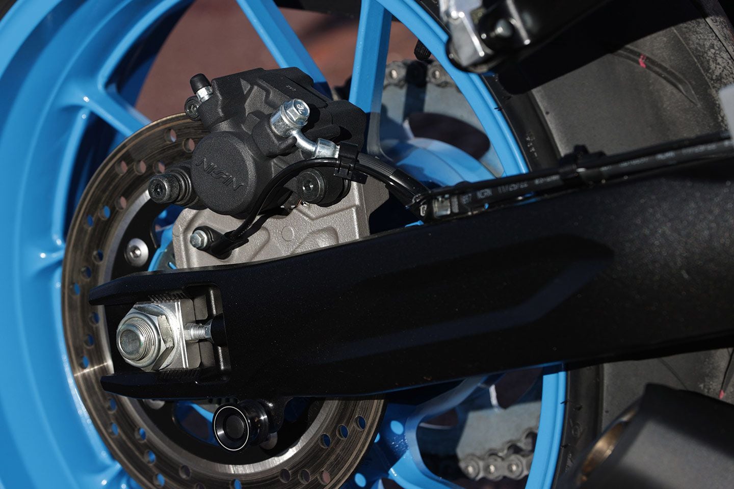 View of the aluminum swingarm and single-piston Nissin rear brake caliper.
