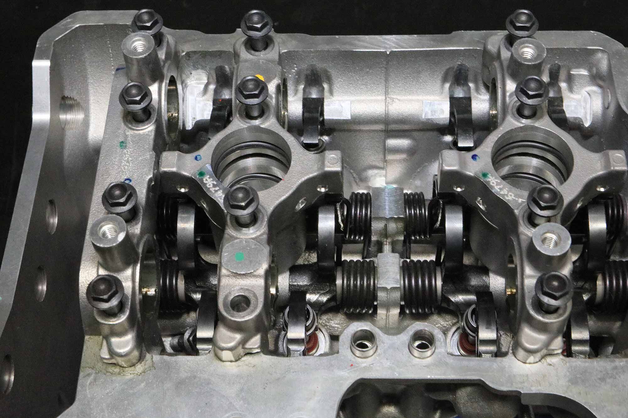 Here we’ve removed the cams, better exposing the opening and closing cam followers. Those hairpin springs are a peculiar component exclusive to the desmo concept; they assist the valve-closing forks and help take up the play between the opening and the closing cams. Eliminating that play altogether would make the desmo system excessively rigid and risk breakage.